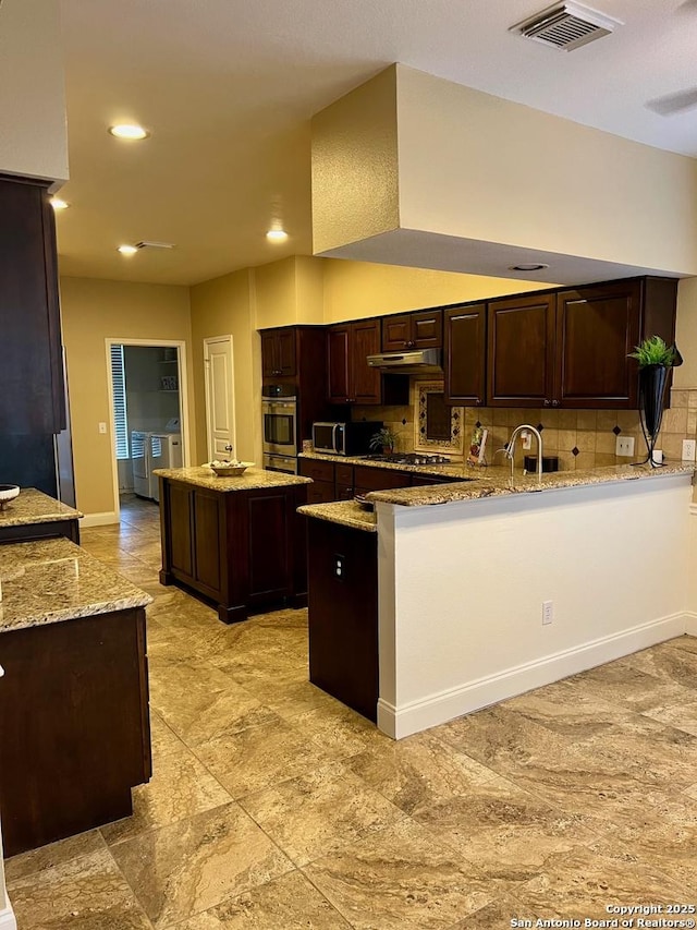 5014 Ashton Audrey, San Antonio, TX 78249 - kitchen with dark brown cabinets, a center island, decorative backsplash, light stone countertops, and a peninsula