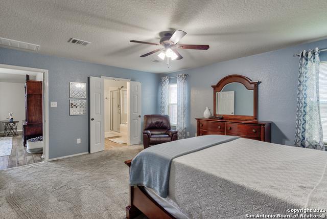 331 Primrose, New Braunfels, TX 78132 - carpeted bedroom featuring a textured ceiling, connected bathroom, a ceiling fan, and baseboards