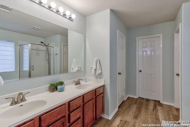 331 Primrose, New Braunfels, TX 78132 - bathroom with wood finished floors, a shower stall, double vanity, a textured ceiling, and baseboards