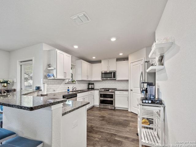 22146 Pivot Pt, San Antonio, TX 78261 - kitchen featuring appliances with stainless steel finishes, a peninsula, decorative backsplash, dark stone countertops, and open shelves