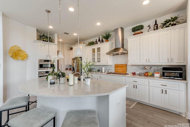 17703 San Felipe Bay, San Antonio, TX 78255 - kitchen featuring wall chimney exhaust hood, a kitchen breakfast bar, light wood finished floors, decorative backsplash, and white cabinets
