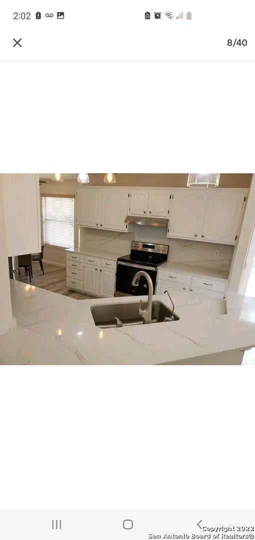 11427 Baltic Dr, San Antonio, TX 78213 - kitchen with electric range, a sink, under cabinet range hood, light stone countertops, and white cabinets