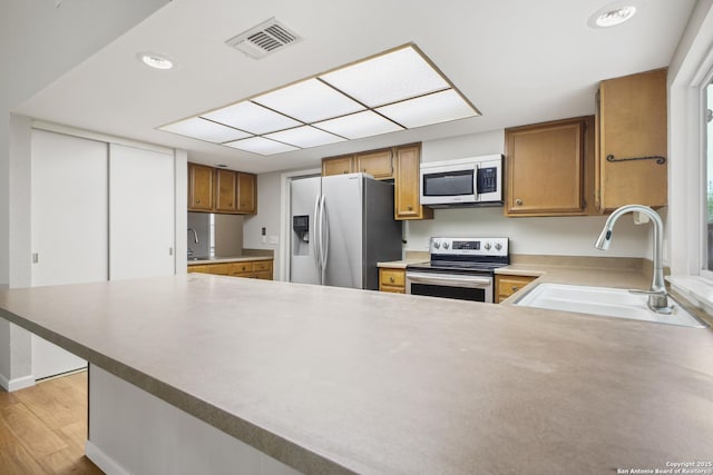11519 Clifton Forge St, San Antonio, TX 78230 - kitchen featuring appliances with stainless steel finishes, a sink, brown cabinetry, a peninsula, and light wood-type flooring