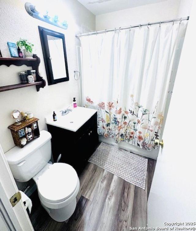 703 Mcdougal, San Antonio, TX 78223 - bathroom with wood finished floors, toilet, vanity, and a shower with shower curtain