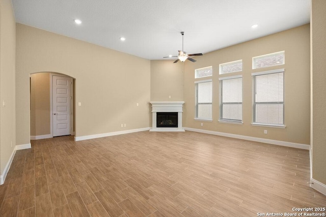 147 Bedingfeld, Shavano Park, TX 78231 - unfurnished living room featuring a ceiling fan, arched walkways, a glass covered fireplace, light wood finished floors, and recessed lighting