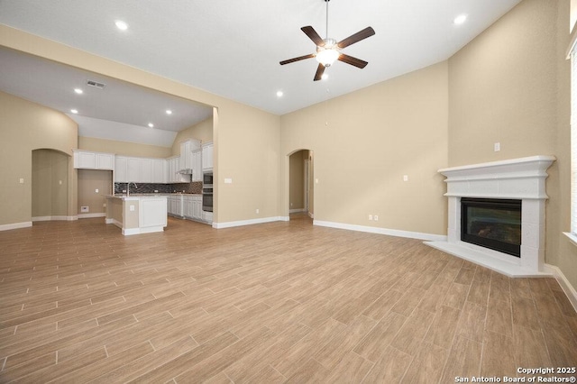 147 Bedingfeld, Shavano Park, TX 78231 - unfurnished living room with lofted ceiling, a ceiling fan, arched walkways, a sink, and baseboards