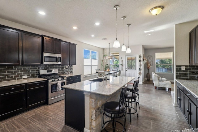 5903 Carriage Cpe, San Antonio, TX 78261 - kitchen with stainless steel appliances, a sink, tasteful backsplash, a center island with sink, and light stone countertops