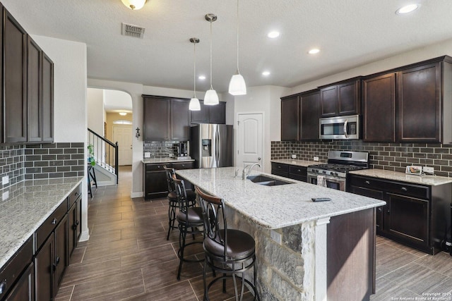 5903 Carriage Cpe, San Antonio, TX 78261 - kitchen with stainless steel appliances, backsplash, a sink, dark brown cabinetry, and light stone countertops