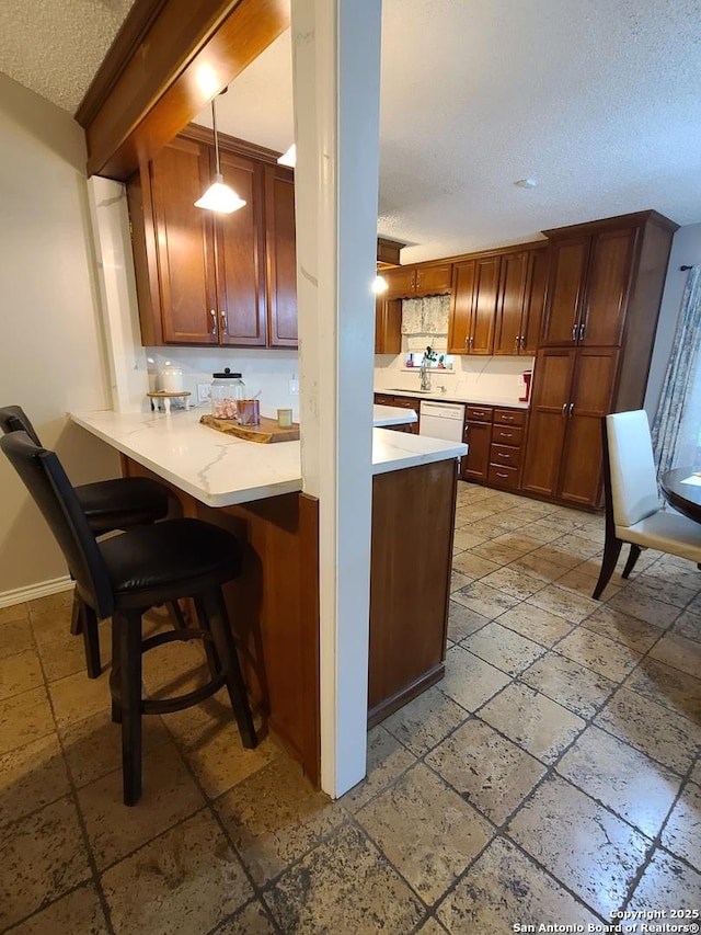 117 Larkspur, Uvalde, TX 78801 - kitchen with a textured ceiling, stone tile flooring, light countertops, a peninsula, and a kitchen breakfast bar