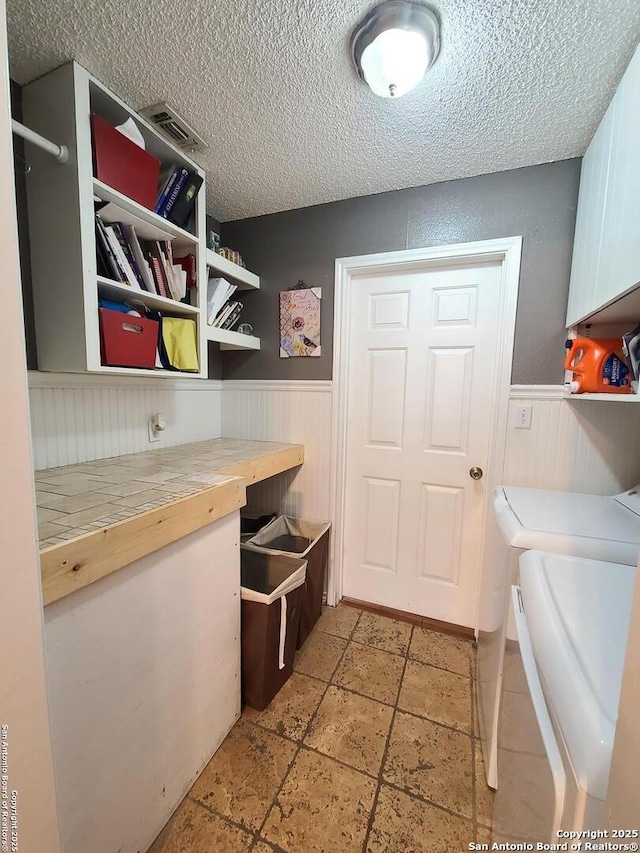 117 Larkspur, Uvalde, TX 78801 - washroom featuring cabinet space, wainscoting, a textured ceiling, washing machine and clothes dryer, and stone tile flooring