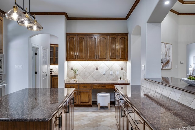 112 Legend Holw, Boerne, TX 78006 - kitchen with arched walkways, backsplash, dark stone countertops, stainless steel microwave, and ornamental molding