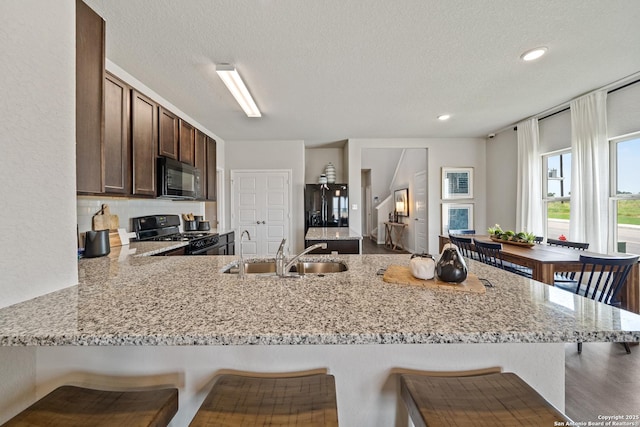9302 Graze Land Dr, San Antonio, TX 78211 - kitchen featuring black appliances, a sink, a peninsula, dark brown cabinetry, and a breakfast bar