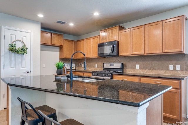 10907 Shoo Fly, San Antonio, TX 78245 - kitchen featuring black microwave, stainless steel gas stove, decorative backsplash, dark stone countertops, and an island with sink