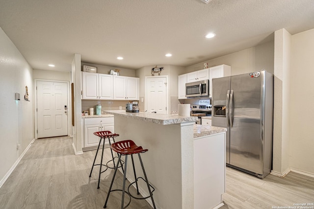 14616 Stable Spgs, Elmendorf, TX 78112 - kitchen with stainless steel appliances, light wood finished floors, a kitchen island, light countertops, and a kitchen bar