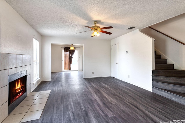 7026 Elmbank, San Antonio, TX 78244 - unfurnished living room featuring wood finished floors, a textured ceiling, a ceiling fan, a tile fireplace, and stairs