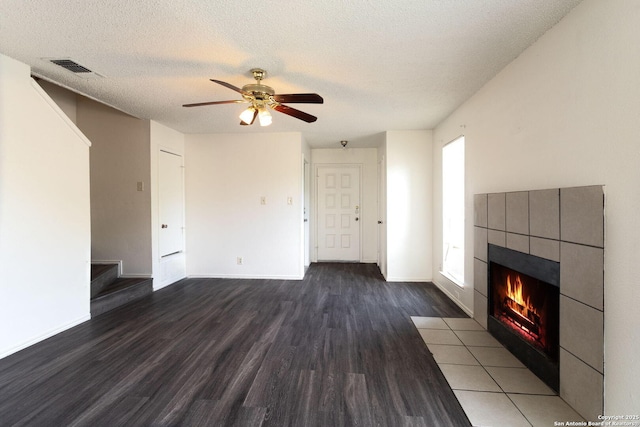 7026 Elmbank, San Antonio, TX 78244 - unfurnished living room with dark wood-style flooring, a tile fireplace, ceiling fan, baseboards, and a textured ceiling