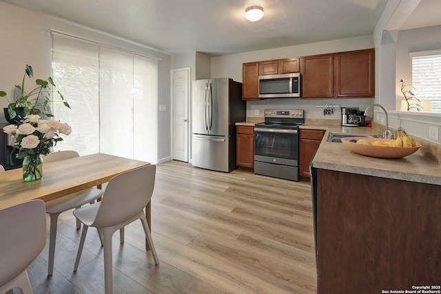 11907 Pure Silver, San Antonio, TX 78254 - kitchen featuring stainless steel appliances, a sink, light wood finished floors, light countertops, and brown cabinets