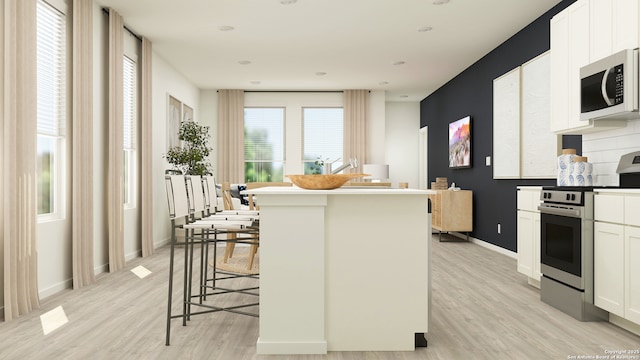 10830 Siebern Rd, San Antonio, TX 78224 - kitchen with appliances with stainless steel finishes, light wood finished floors, white cabinets, a center island, and baseboards