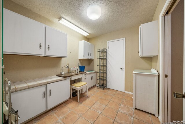 11 El Norte Cir, Uvalde, TX 78801 - kitchen with a textured ceiling, white cabinets, and tile counters