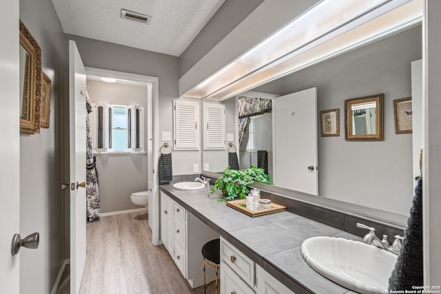 11 El Norte Cir, Uvalde, TX 78801 - full bath with double vanity, toilet, wood finished floors, a textured ceiling, and baseboards