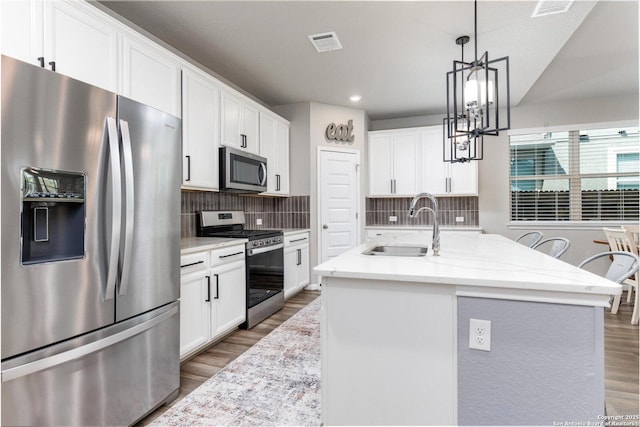 2331 Greystone Lndg, San Antonio, TX 78259 - kitchen with stainless steel appliances, wood finished floors, a chandelier, white cabinets, and decorative backsplash