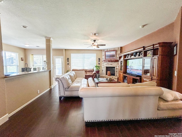 1031 Starlit Pond, San Antonio, TX 78260 - living room with a ceiling fan, a large fireplace, dark wood-type flooring, baseboards, and a textured ceiling