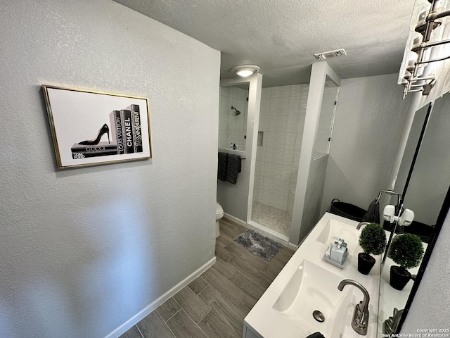 6422 Balky St, San Antonio, TX 78240 - bathroom with a walk in shower, wood finish floors, double vanity, baseboards, and a textured ceiling