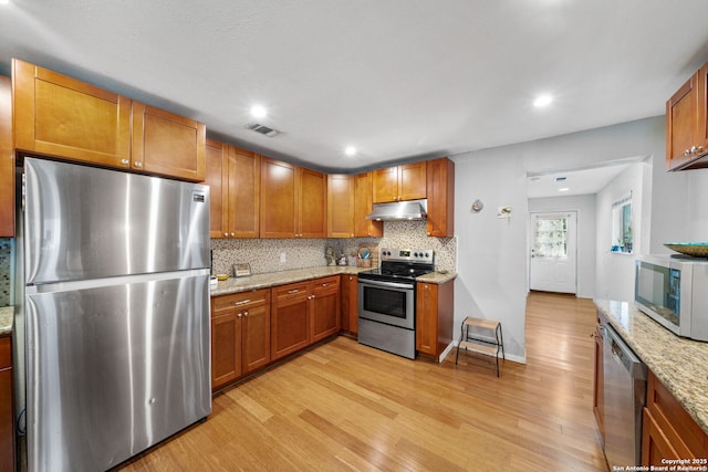 1119 N Pine St, San Antonio, TX 78202 - kitchen featuring appliances with stainless steel finishes, under cabinet range hood, light wood-type flooring, tasteful backsplash, and brown cabinets