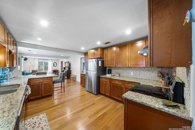 1119 N Pine St, San Antonio, TX 78202 - kitchen featuring freestanding refrigerator, wall chimney range hood, light wood-style floors, light stone counters, and tasteful backsplash