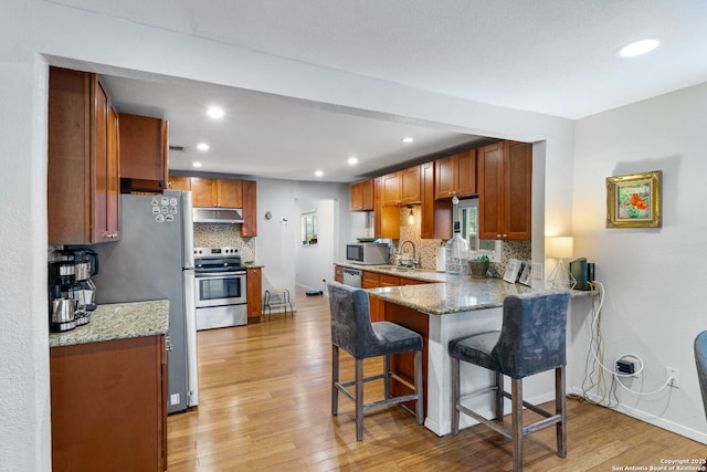 1119 N Pine St, San Antonio, TX 78202 - kitchen with stainless steel appliances, under cabinet range hood, a sink, light wood-style floors, and a peninsula