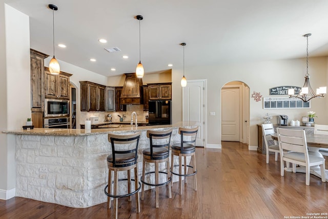 311 Wentworth, Spring Branch, TX 78070 - kitchen with appliances with stainless steel finishes, arched walkways, premium range hood, light stone counters, and tasteful backsplash