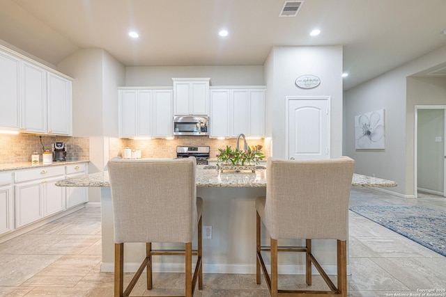 2705 Merlin Ln, Pearland, TX 77581 - kitchen with appliances with stainless steel finishes, a breakfast bar area, a center island with sink, light stone counters, and recessed lighting