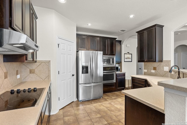 9815 Leubeck Rnch, Helotes, TX 78023 - kitchen featuring appliances with stainless steel finishes, arched walkways, a sink, under cabinet range hood, and dark brown cabinets