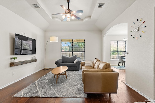 9815 Leubeck Rnch, Helotes, TX 78023 - living room with dark wood-style flooring, arched walkways, a tray ceiling, a ceiling fan, and baseboards