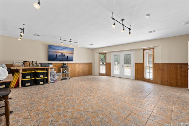 585 Oak Bend Dr, Bandera, TX 78003 - unfurnished living room with a wainscoted wall, wooden walls, track lighting, stone finish floors, and french doors