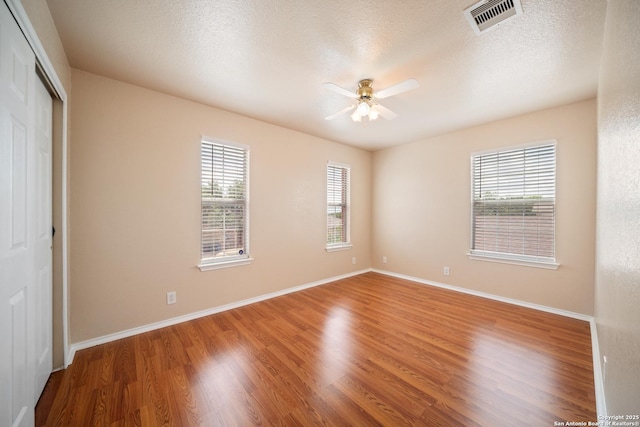 7731 Cedar Farm, San Antonio, TX 78239 - unfurnished bedroom with multiple windows, wood finished floors, a closet, baseboards, and a textured ceiling