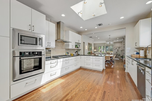 106 Mayflower, Alamo Heights, TX 78209 - kitchen with appliances with stainless steel finishes, wall chimney range hood, light wood finished floors, a peninsula, and dark countertops