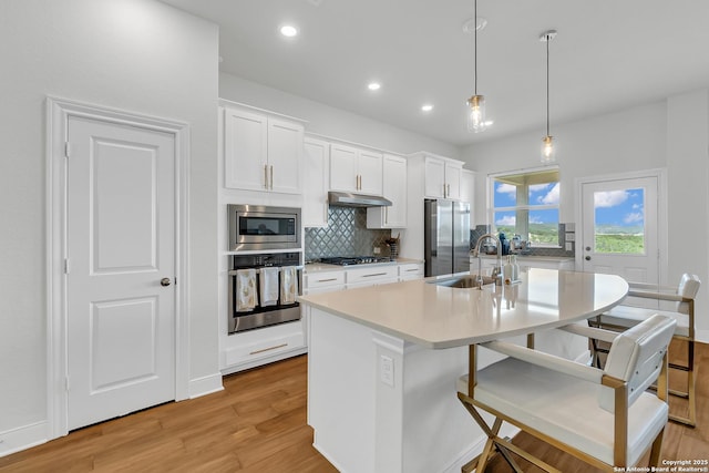 6827 Bella Verso, San Antonio, TX 78256 - kitchen featuring stainless steel appliances, a sink, light wood-style flooring, tasteful backsplash, and a kitchen island with sink