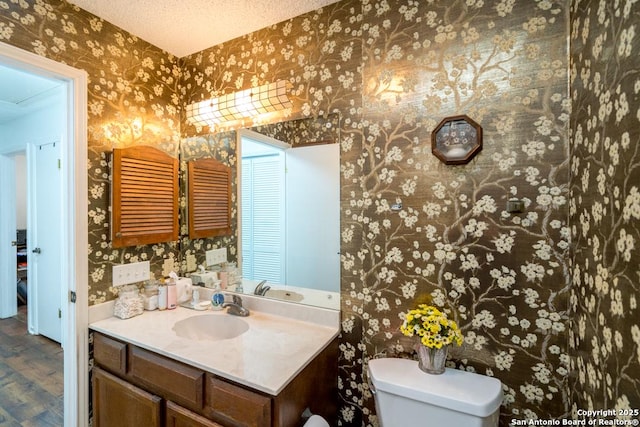 5823 Archwood, San Antonio, TX 78239 - half bath featuring wallpapered walls, vanity, toilet, wood finished floors, and a textured ceiling