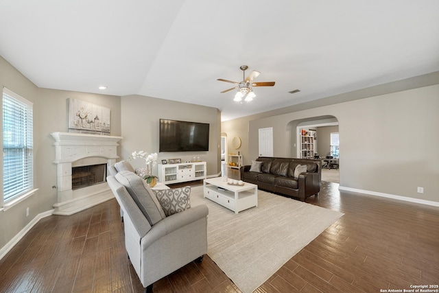 13014 Essen, Helotes, TX 78023 - living room featuring arched walkways, ceiling fan, dark wood finished floors, a fireplace with raised hearth, and baseboards