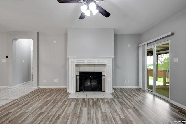 1947 Walter Raleigh, Windcrest, TX 78239 - unfurnished living room with light wood-style floors, ceiling fan, arched walkways, a fireplace, and baseboards