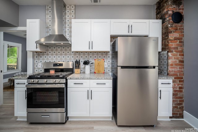 128 Blanco, San Antonio, TX 78212 - kitchen featuring appliances with stainless steel finishes, wall chimney exhaust hood, light stone countertops, and light wood-style flooring