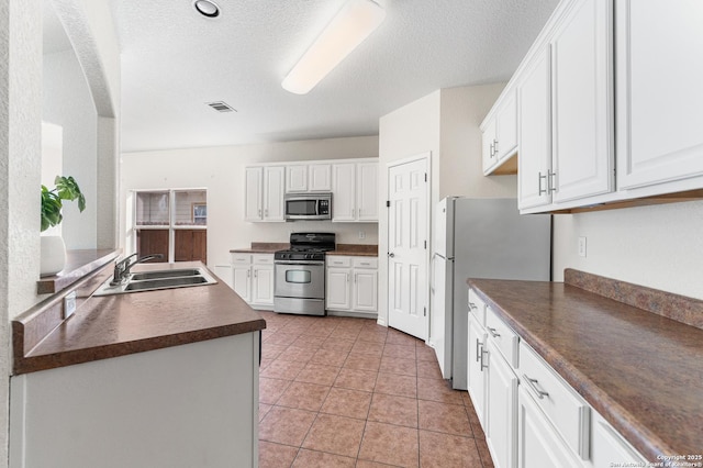 7619 Bit Cir, Elmendorf, TX 78112 - kitchen featuring stainless steel appliances, dark countertops, a sink, white cabinets, and a textured ceiling