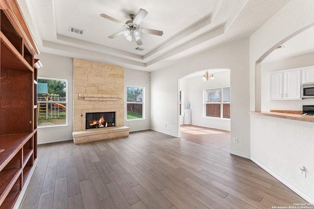 7619 Bit Cir, Elmendorf, TX 78112 - unfurnished living room featuring a tray ceiling, arched walkways, plenty of natural light, and wood finished floors
