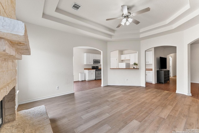 7619 Bit Cir, Elmendorf, TX 78112 - unfurnished living room with a tray ceiling, ceiling fan, light wood-style flooring, a stone fireplace, and baseboards