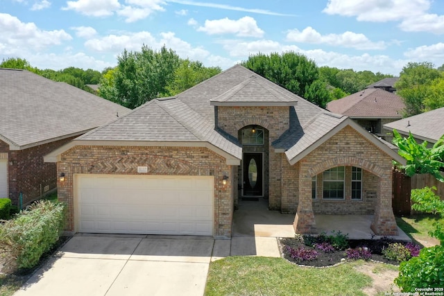 8022 Grissom Crst, San Antonio, TX 78251 - french country style house with brick siding, a garage, driveway, a shingled roof, and stone siding