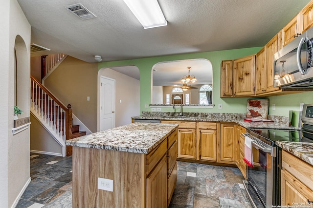 8227 Maloy Mnr, San Antonio, TX 78250 - kitchen featuring stainless steel appliances, stone tile floors, arched walkways, a center island, and a textured ceiling