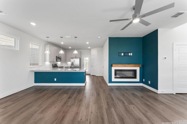 9607 Stillwater Pass, San Antonio, TX 78254 - kitchen with appliances with stainless steel finishes, a glass covered fireplace, a peninsula, dark wood-style floors, and light countertops