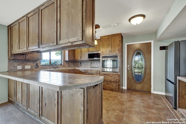 642 Lakebreeze, Canyon Lake, TX 78133 - kitchen featuring stainless steel appliances, tile countertops, a peninsula, tasteful backsplash, and brown cabinets
