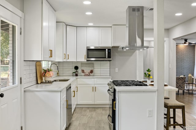 207 Northaven, San Antonio, TX 78229 - kitchen featuring appliances with stainless steel finishes, a sink, island range hood, light wood-type flooring, and recessed lighting